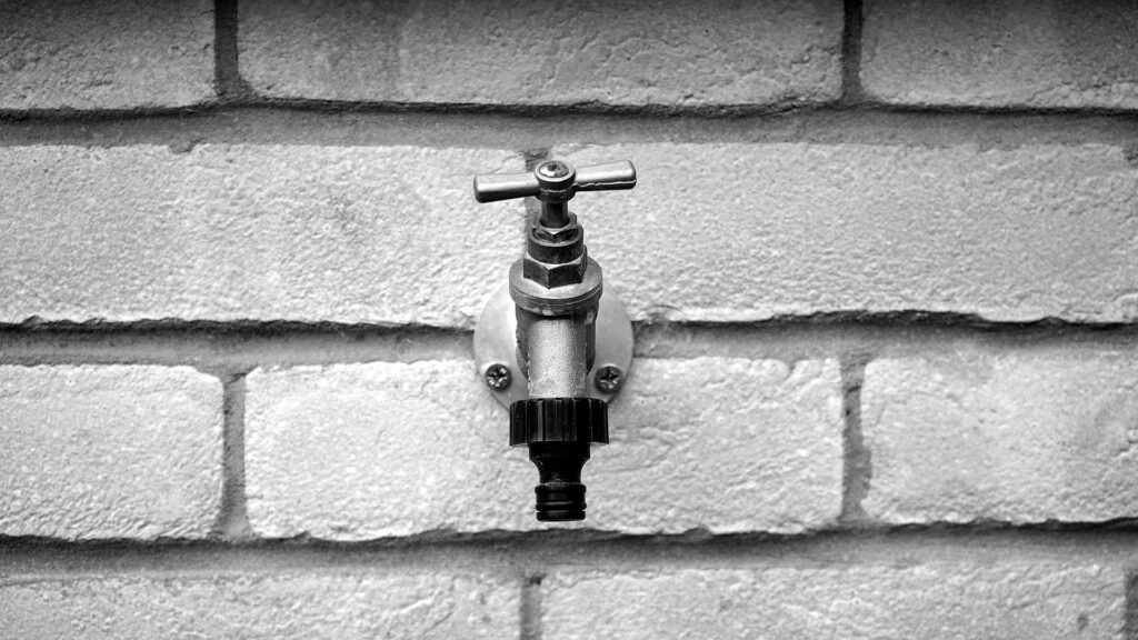 A photo of an old hose bib with a brick wall behind it