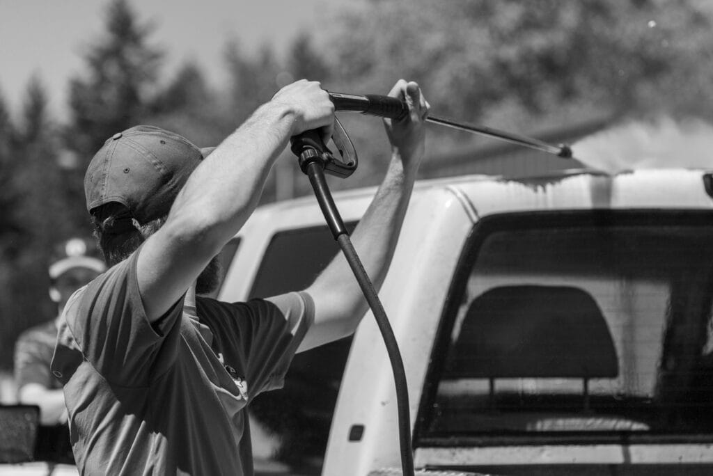 a man cleans off oil from his truck using hot water